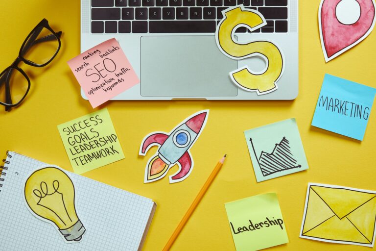 top view of laptop, paper signs and paper stickers with business plan on yellow surface